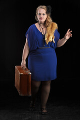Fat woman dressed in the style of the 20-30s of the last century with a suitcase on a dark...