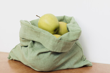 Fresh apples in eco cotton bag on wooden table. Zero waste shopping. Fruits in reusable green bag
