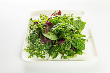 salad mix of fresh herbs, arugula, chard, spinach in a plate on a white plate, top-side view