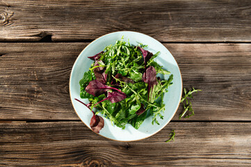 salad mix of fresh herbs, arugula, Swiss chard, spinach in tarenle on a wooden background, serhu view