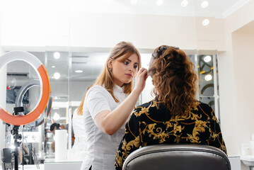 In a beautiful, modern beauty salon, a professional makeup stylist makes makeup for a young girl....
