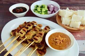 Indonesian chicken satay or Sate Ayam  with lontong. Served with sweet soy sauce, peanut sauce and pickles cucumber and onion