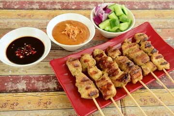 Indonesian chicken satay or Sate Ayam. Served with sweet soy sauce, peanut sauce and pickles cucumber and onion