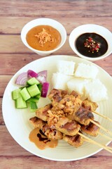 Indonesian chicken satay or Sate Ayam  with lontong. Served with sweet soy sauce, peanut sauce and pickles cucumber and onion