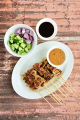 Indonesian chicken satay or Sate Ayam. Served with sweet soy sauce, peanut sauce and pickles cucumber and onion