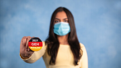 Junge Frau mit braunem Haar und gelben Pulli streckt den Arm aus und hält einen Button in den...