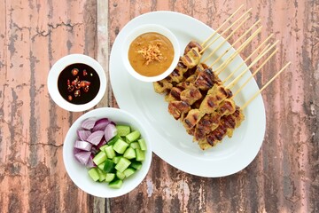 Indonesian chicken satay or Sate Ayam. Served with sweet soy sauce, peanut sauce and pickles cucumber and onion