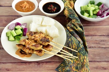 Indonesian chicken satay or Sate Ayam  with lontong. Served with sweet soy sauce, peanut sauce and pickles cucumber and onion