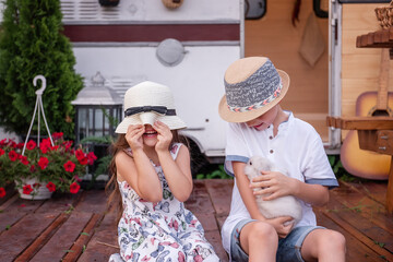 Boy and girl are having fun at trailer truck home on wooden floor, holding fluffy rabbit bunny in...