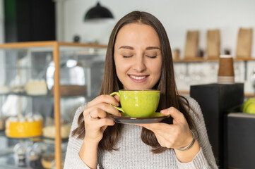 Smiling woman with eyes closed enjoys a morning coffee sitting in the cozy cafe, a calm female with cup of hot drinks indoor