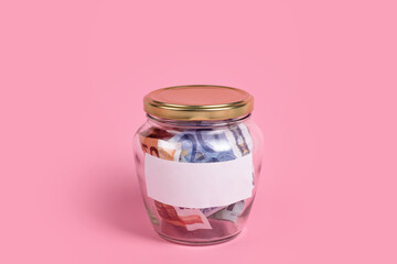 Euro banknotes in glass money jar with blank label, financial, saving. Money box with empty sticky note paper. Jar full of cash, save money concept, expense planning and control, free space for text