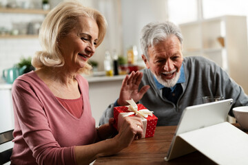 Senior couple having video call. Happy husband giving his wife a gift..