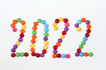 2022, colorful smarties on white background. Chocolate candies in shape of buttons, top view.