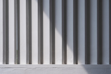 White wooden sunshade battens on cement wall with sunlight and shadow on surface