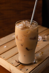 In a glass filled to the top with ice and coffee with milk. A glass of iced coffee sits on a crate against a wooden background.