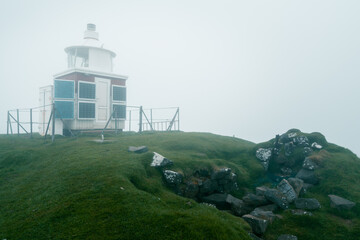 Kalsoy island lighthouse, barely visible in a thick mist surrounding it. Very cloudy, misty day in Kalsoy, Faroes.