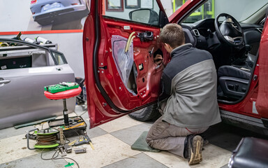 Mechanic guy in automobile service stay on a knees near car door at time of it dismantling to repair car after road accident