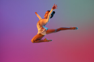 Fototapeta na wymiar African-american rhythmic gymnast, pretty girl practicing on gradient studio background in neon light