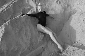 Full length portrait of a sensual young woman with blonde hair, dresses in bodysuit smoking, posing on the sand.