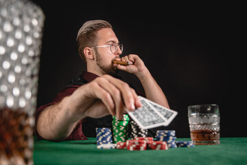 Young gentleman smoking cigar while playing poker with whisky in glass