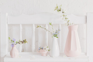 cups and vases with spring flowers on vintage wooden white shelf