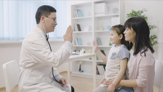 Doctor listening asian girl with stethoscope giving high five, treatment success