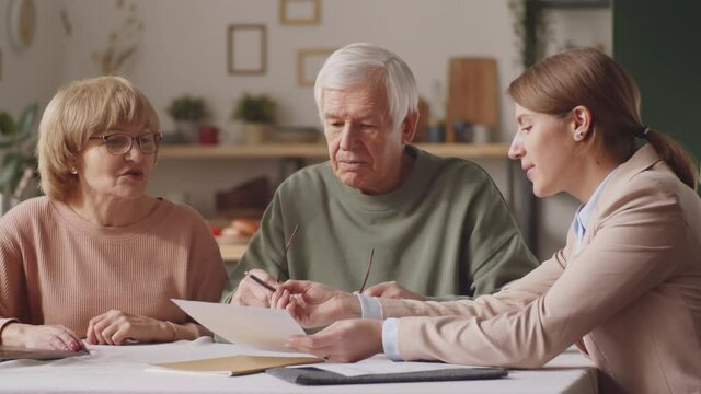 Female financial advisor explaining document to elderly couple as giving consultation about savings and investments at home
