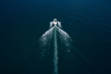 Drone view of a boat. Top view of a white boat sailing to the blue sea. Yacht in the rays of the sun on blue water.  Aerial view luxury motor boat.