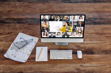 Distance learning, online education. A monitor with a group of international people stands on a wooden table. Woman teacher conducts online lesson for students, shows information on a whiteboard