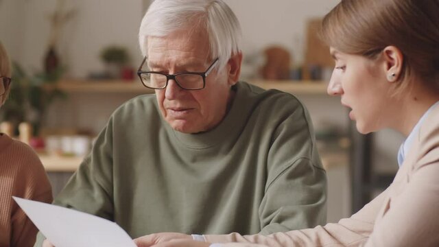 Elderly family couple going through papers and having discussion about investments with female financial consultant during meeting at home