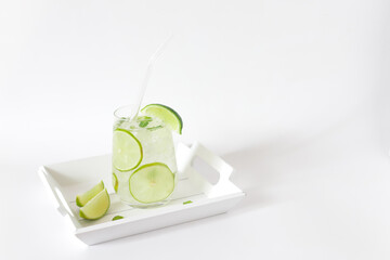 Glass of cold water with fresh lime and ice with glass straw in small white wooden tray.
