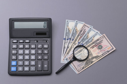  Inflation, exchange rate differences of world currencies. Insurance. Banknotes of 50 and 100 US dollars on a dark gray background with a magnifying glass and a calkulator.Horizontal photo, top view. 