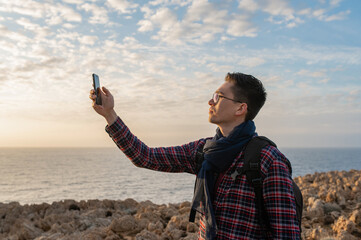Young male in a remote location on a rocky cliff with sea on background. Man holding smartphone trying to catch signal.