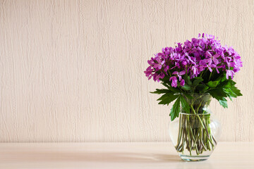 Beautiful delicate purple wildflowers in glass vase on the table with copy space. Minimalistic home decor. Floral background