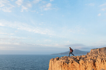 Fototapeta premium Young hiker man walking on a high jagged cliff overhanging the sea.