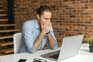Worried guy looks at laptop screen anxiously cover face with palms, found a mistake in a report, an office employee fails to complete the work before the deadline