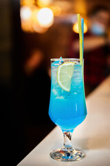 Blue alcoholic cocktail with orange, ice and straw. Close-up, selective focus