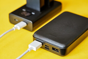Power bank charges batteries using a USB cable on a yellow background. Close-up, selective focus