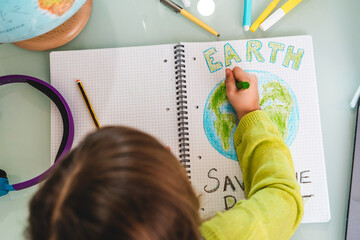 Top view of child girl draws planet earth with wax colors on school notebook for Earth day - Little...