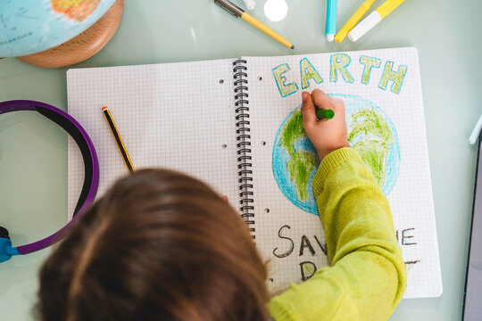 Top view of child girl draws planet earth with wax colors on school notebook for Earth day - Little activist girl writes the message Save the Planet - Protection of environment, global warming