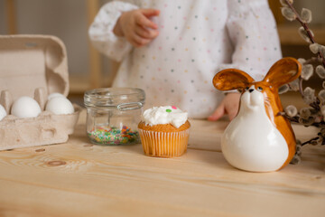Cute little girl in a cotton dress at home in a wooden kitchen prepares an Easter cake