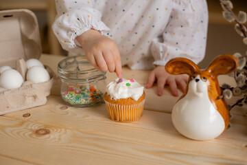 Cute little girl in a cotton dress at home in a wooden kitchen prepares an Easter cake