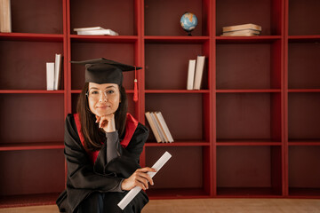 brunette student in glasses, graduation cap and gown holding diploma