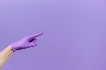 Male finger pointing at copy space, wears medical protective latex gloves, isolated on purple studio background wall with copy space for advertisement. Advertising area, mockup. Hand gesture concept