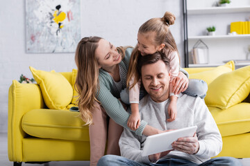 Smiling woman looking at daughter hugging father with digital tablet.