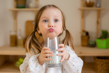 A cute little girl drinks milk at home in a wooden kitchen. Milk Day
