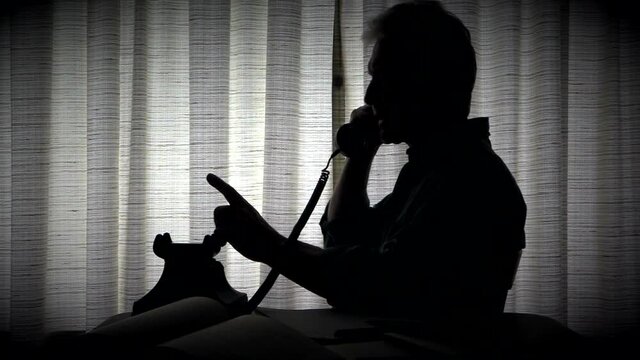 Man in silhouette talking on land line telephone black and white