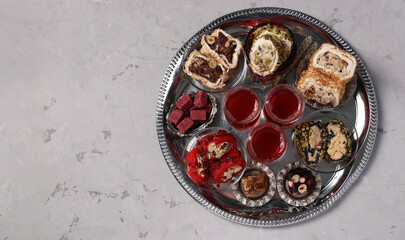 Tea ceremony with an assortment of Turkish sweets on a round metal tray on a gray background. View from above. Space for text