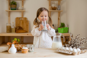 A cute little girl drinks milk at home in a wooden kitchen. Milk Day