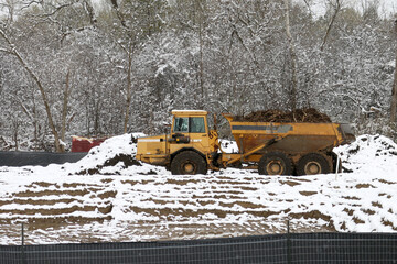 Excavator filling dumptruck in early spring snowfall in construction sight on overcast spring day